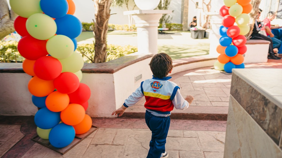 Boy in paw patrol jacket runs past colorful balloons